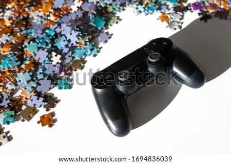 Scattered jigsaw puzzle pieces in natural colors and black game controller. Lying on white table. Concept of traditional entertainment versus modern game.