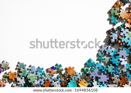 Top view of scattered multicolored jigsaw puzzle pieces. Lying on white table arranged as frame for copy space. Concept of putting together disconnect elements.