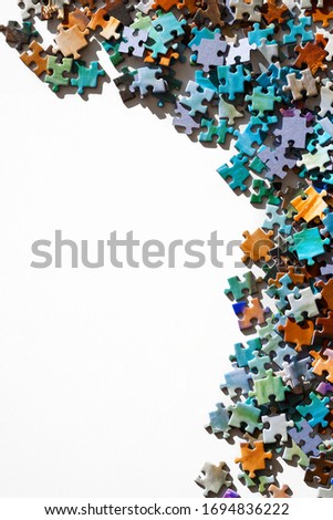 Top view of scattered multicolored jigsaw puzzle pieces. Lying on white table arranged as frame for copy space. Concept of putting together elements. Vertical photo.