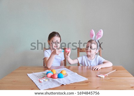 Cute little baby in pink toy ears playing with Easter eggs on Easter day. Colorful eggs on a wooden surface