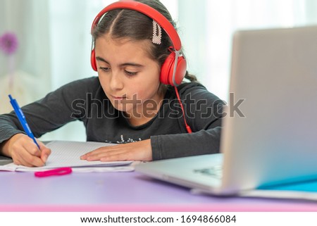Home Schooling. Learning from home in coronavirus times. Young girl hearing school lesson in her headphones connected with laptop while doing homework.