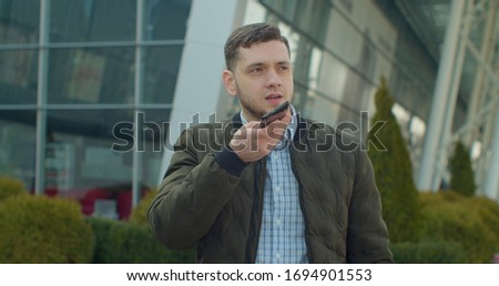 Man using a smartphone voice recording function online walking on a city street, talking to mobile assistant. Man using smartphone voice recognition, dictates thoughts, voice dialing message.