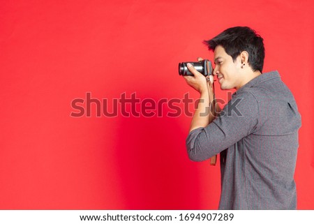 Young Asian hipster man searching for an interesting subject on the studio on a red background.Travel Lifestyle concept