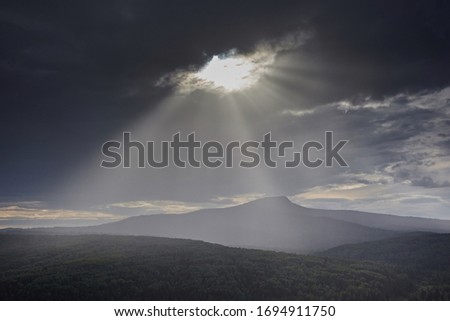 The sun's rays make their way through the clouds and the gloomy sky against the silhouette of the mountain. Minimalist landscape
