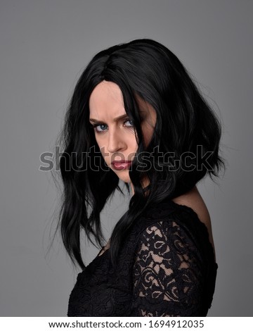 Close up portrait of a pretty, goth girl with dark hair  posing in front  a studio background.