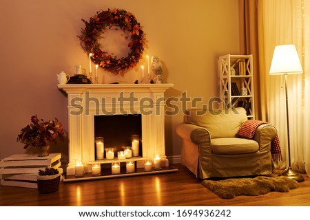 Fireplace, chair and floor decorated autumn wreath. Night windows at the background. Autumn interior in a cozy hous