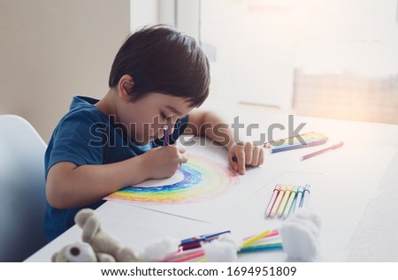 Kid using colour pen painting rainbow on paper,Child using digital tablet searching information on internet about rainbow color, Home schooling Social media campaign for coronavirus prevention concept