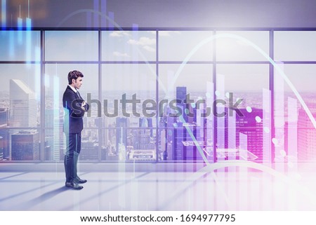 Confident young businessman standing in panoramic office with double exposure of blurry financial graph. Concept of stock market and leadership. Toned image
