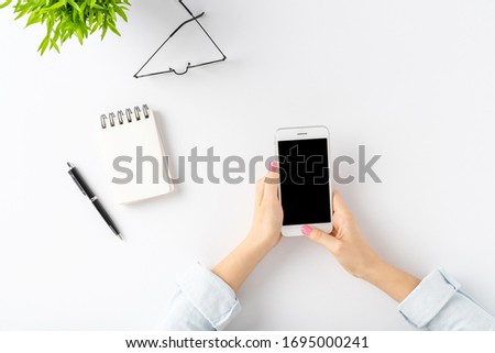 Young woman using mobile phone over white table. Office desktop. Top view