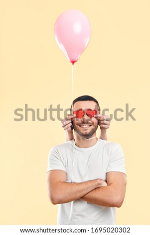 Weird funny man with small paper hearts by their eyes and pink air balloon on his neck on beige background