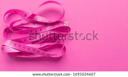 Pink centimeter on pink background. Simple flat lay with pastel texture. Fitness concept. Stock photo.