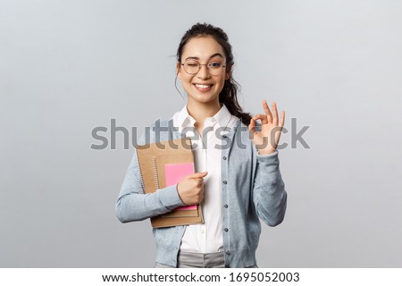 Education, teachers, university and schools concept. Girl guarantee you will like this language courses. Cheerful smiling asian woman show okay sign and wink, recommend study her, hold notebooks