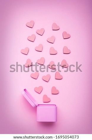 Pink round metal gift box with small wooden hearts on a delicate pink background. Top view