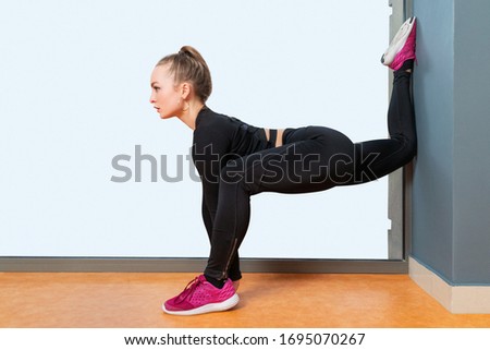 Woman doing splits with one foot leaning against a wall, isolated against a white window