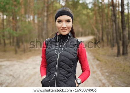 Caucasian girl is walking in a beautiful forest at the weekend. She is listening 
favorite music. She has a beautiful smile. She is looking into the lens. Healthy lifestyle and relax concept.