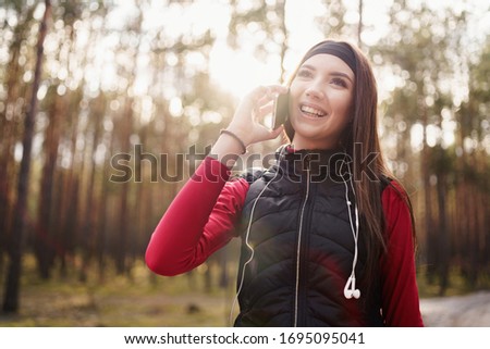 Teenager girl is walking in a pine forest at the weekend. She is talking to her friend on the phone. She has a beautiful smile. Healthy lifestyle concept.