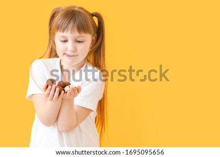 Cute little girl with chocolate candies on color background