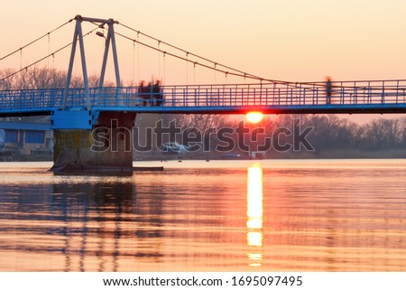 A suspension footbridge with motion blurred people silhouettes at the sunrise.