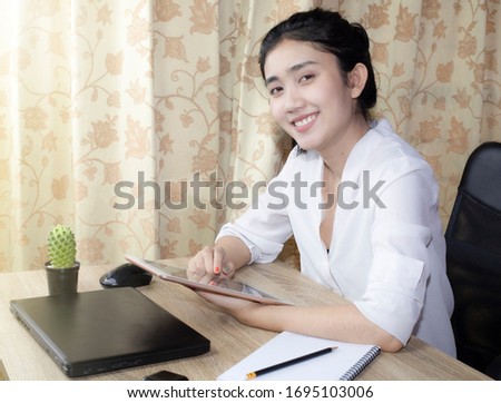 Asian woman is sitting and searching for work-related information on an iPad at her home desk on Monday morning before work.