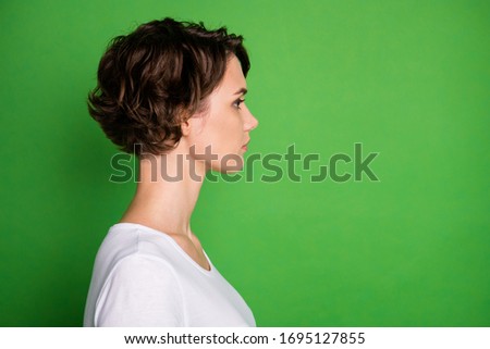 Closeup profile photo of attractive lady short wavy hairdo not smiling look side empty space concentrated wear casual white t-shirt isolated green color background