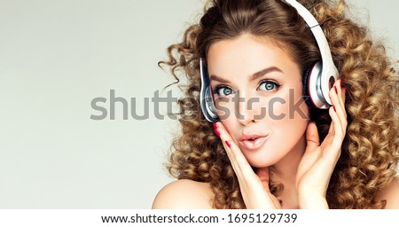 Beautiful smiling girl , afro curly hair listening and enjoying to music with headset . Joyful woman in big wireless headphones . Electrical goods and accessories. Sound and melody for a good mood.