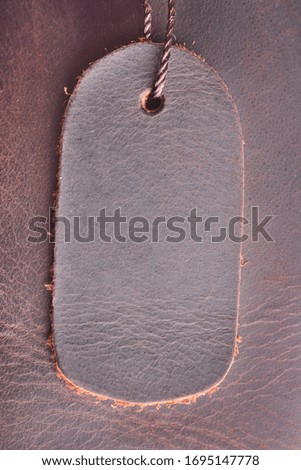 Tag, a label made of genuine leather on a new product, dark brown on a background of leather texture, close-up
