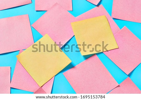 Scattered yellow and many pink square blank paper stickers on blue background. Copy space