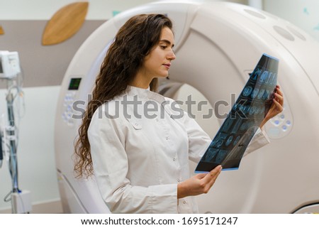 The young women doctor in medical gown looks at x-ray picture of patient brain after computer tomography. CT diagnostic in medical clinic