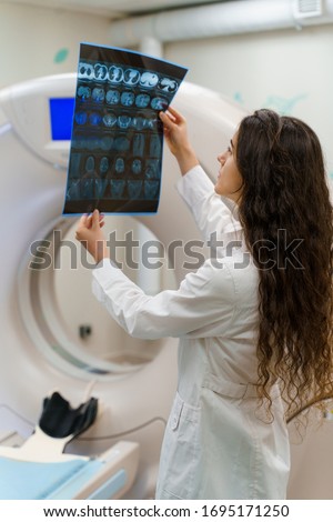 Vertical picture of medical student who looks at x-ray picture of patient brain near kt komputer tomograhphy. Young girl in medical clinic gotes new expirience