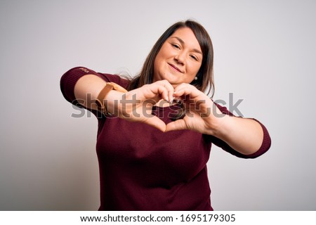 Beautiful brunette plus size woman wearing casual sweater over isolated white background smiling in love doing heart symbol shape with hands. Romantic concept.