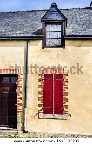 Old house wall facade, wooden brown door and red shutters, France. Traditional typical style of brittany house exterior. 