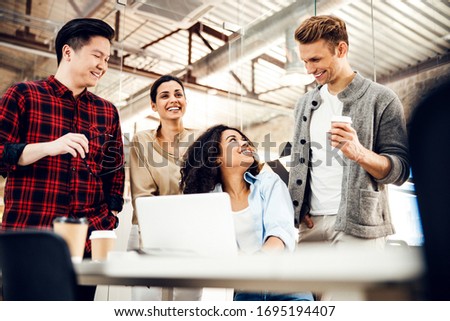Group of joyful multiracial people using notebook, chatting and laughing in office stock photo