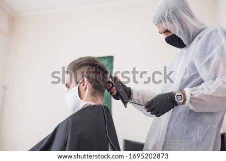 The work of the barber during the coronavirus, the hairdresser trim the client in a mask and a protective suit, quarantine Royalty-Free Stock Photo #1695202873