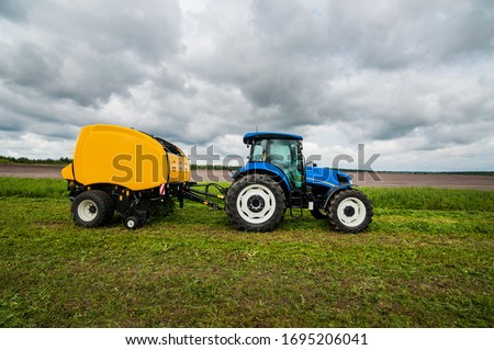 new blue tractor with Baler in motion in farm work at field with green grass