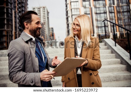 Joyful male broker with a clipboard in his hand looking at a smiling female buyer