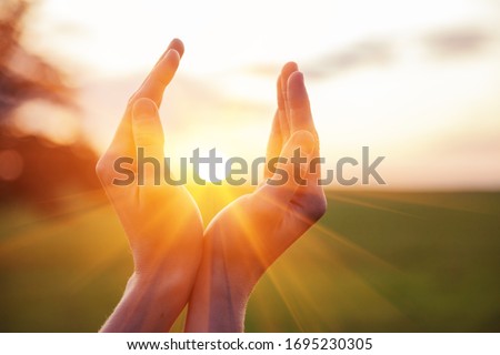 young woman raising hands praying at sunset or sunrise light Royalty-Free Stock Photo #1695230305