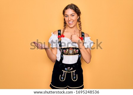 Young beautiful blonde german woman with blue eyes wearing traditional octoberfest dress Showing palm hand and doing ok gesture with thumbs up, smiling happy and cheerful