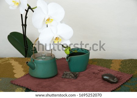 Still life with tea utensils and white orchid flower. Translation of chinese hieroglyph on napkin: "Tea rhyme"