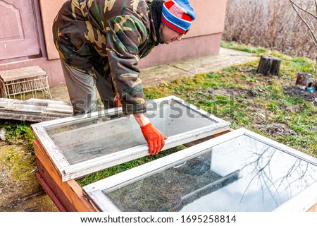 Man working on diy project construction closeup of vegetable winter garden for raised bed cold frame box in Ukraine dacha by farm house Royalty-Free Stock Photo #1695258814
