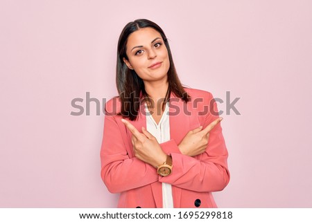 Young beautiful brunette businesswoman wearing elegant jacket over isolated pink background Pointing to both sides with fingers, different direction disagree