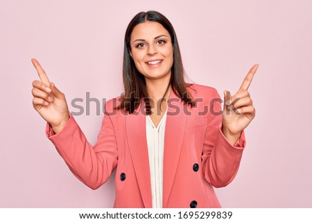 Young beautiful brunette businesswoman wearing elegant jacket over isolated pink background smiling confident pointing with fingers to different directions. Copy space for advertisement