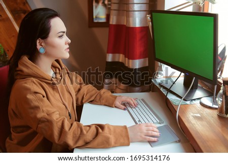 The girl is sitting at home at the desk. Computer with a green screen. Home schooling, freelance, girl sitting at home at the computer.