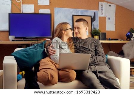 A couple is sitting on a couch and looking at a computer. The couple watches movies together, works, creates a project, freelance, looks at the computer, smiles.