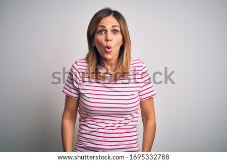 Middle age beautiful woman wearing casual striped t-shirt over isolated white background afraid and shocked with surprise expression, fear and excited face.