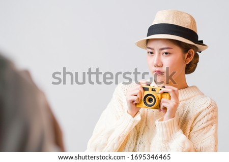 Cute young Asian tourist woman holding camera in her hand with thinking expression on her face isolated in grey background with copy space, negative expression, Explore and think before shoot concept.