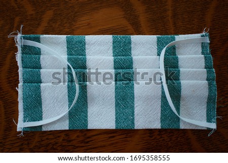 homemade cotton face mask with three pleats, elastic, and green and white fabric