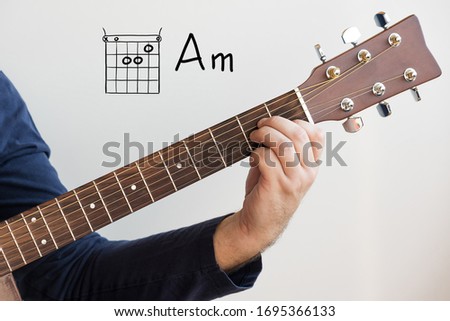 Learn Guitar - Man in a dark blue shirt playing guitar chords displayed on whiteboard, Chord A minor (Am) Royalty-Free Stock Photo #1695366133