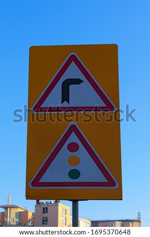 Road turn right sign and Traffic light ahead sign. Two road signs on big yellow plate. Blurred residential building and blue sky in the background. Concept of road sign. Kyiv, Ukraine.