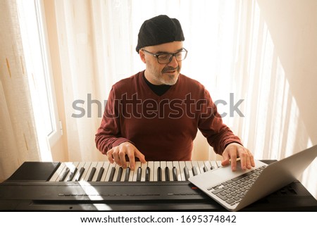 A man learning to play piano online with a computer staying at home. Concepts of self taught, staying at home and working online Royalty-Free Stock Photo #1695374842