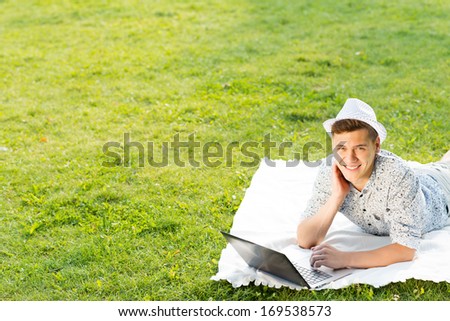 young man in the park sitting on the grass, enthusiastically working with a laptop